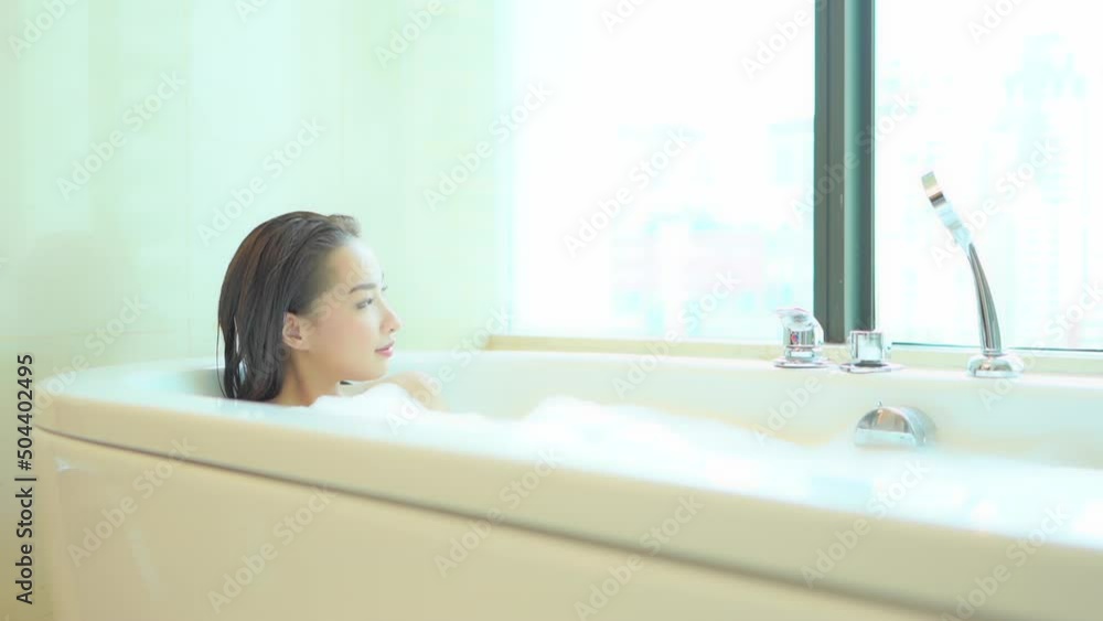 A pretty woman relaxes in a bubble bath as she looks out of her high-rise window. A pretty woman relaxes in a bubble bath as she looks out of her high-rise window.