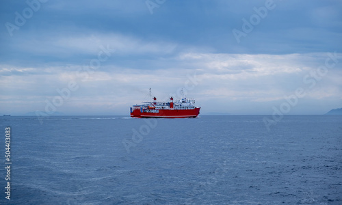 Red ferry boat on rippled sea, blue cloudy sky. Transportation in Meditteranean Sea