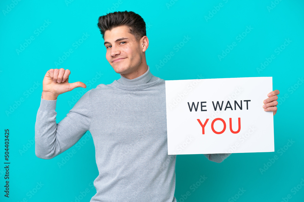 Young handsome caucasian man isolated on blue bakcground holding We Want You board with proud gesture Young handsome caucasian man isolated on blue bakcground holding We Want You board with proud gesture