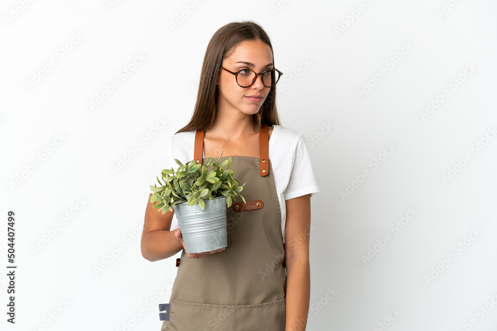 Gardener girl holding a plant over isolated white background looking to the side Gardener girl holding a plant over isolated white background looking to the side