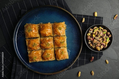 Delicious sweet baklava with pistachios on black table, flat lay