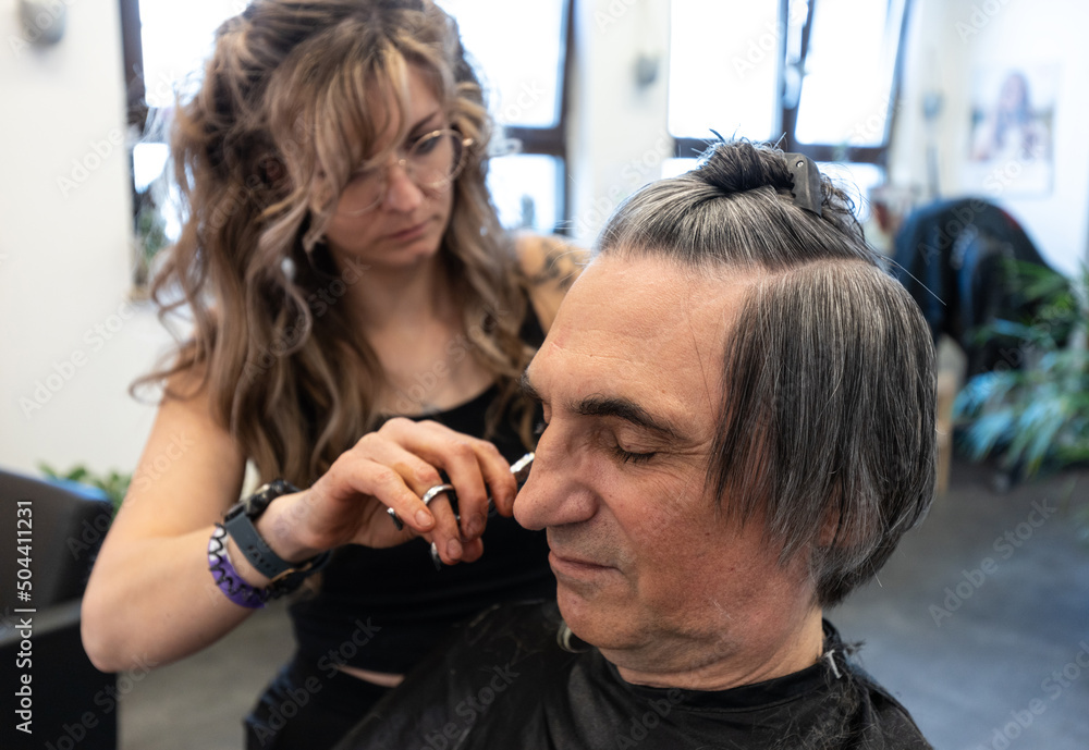 Fototapeta premium The hairdresser cuts the hair of an elderly client in his own salon