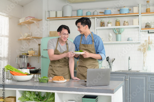 Young smiling gay couple cooking together in the kitchen at home, LGBTQ and diversity concept.