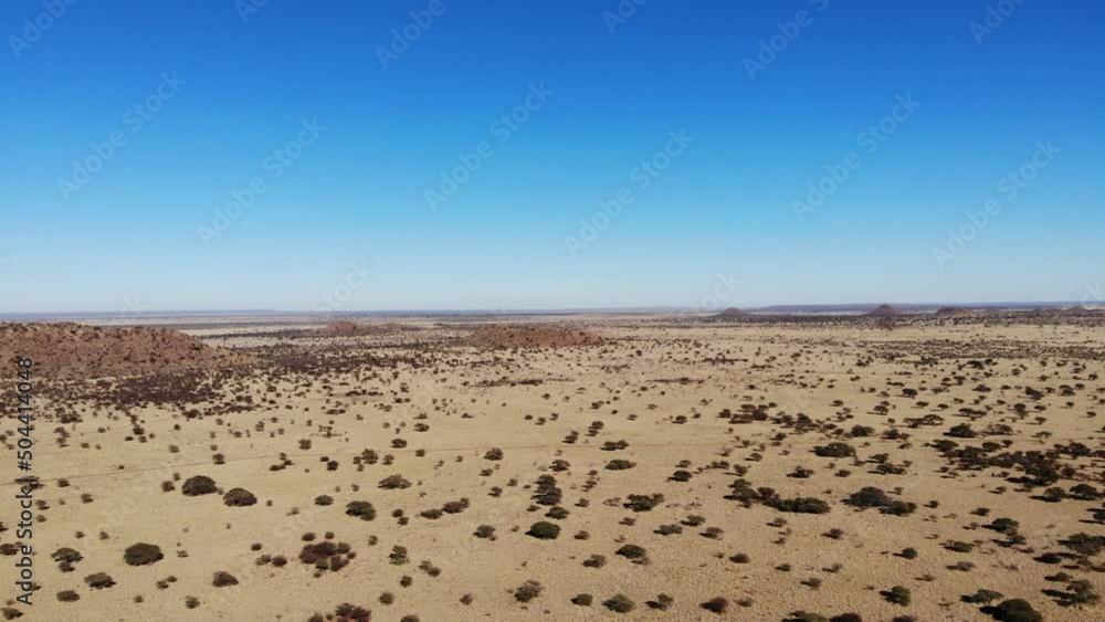 An extreme long shot that pans across a dry, desert environment. The shot shows a vast sandy landscape with little vegetation as well as small brown hills against a clear blue sky. An extreme long shot that pans across a dry, desert environment. The shot shows a vast sandy landscape with little vegetation as well as small brown hills against a clear blue sky.