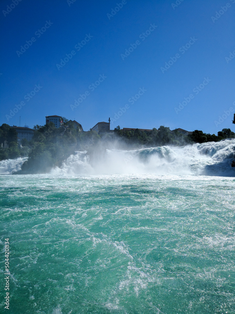 Beautiful view of the Rhine Falls against the blue sky. Rushing streams of water raise splashes into the air. Vertical. Rheinfalls, Switzerland