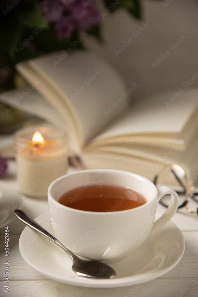 A cup of green tea against the background of a spring bouquet of lilacs on a textured gray background.Romantic composition with books and candles. Spring tea drink. Side view. Place to copy.