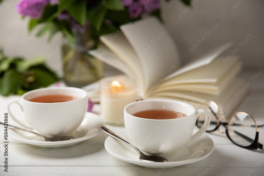 A cup of green tea against the background of a spring bouquet of lilacs on a textured gray background.Romantic composition with books and candles. Spring tea drink. Side view. Place to copy. A cup of green tea against the background of a spring bouquet of lilacs on a textured gray background.Romantic composition with books and candles. Spring tea drink. Side view. Place to copy.