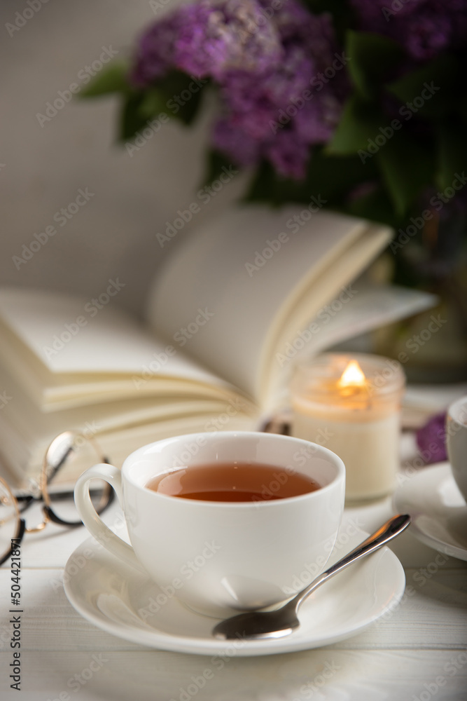 A cup of green tea against the background of a spring bouquet of lilacs on a textured gray background.Romantic composition with books and candles. Spring tea drink. Side view. Place to copy. A cup of green tea against the background of a spring bouquet of lilacs on a textured gray background.Romantic composition with books and candles. Spring tea drink. Side view. Place to copy.
