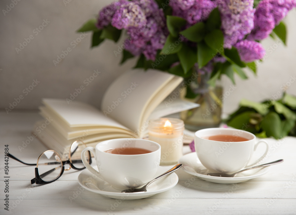 A cup of green tea against the background of a spring bouquet of lilacs on a textured gray background.Romantic composition with books and candles. Spring tea drink. Side view. Place to copy.