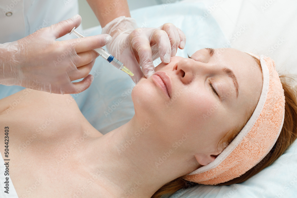 Cosmetologist performs the chin lift procedure by injecting beauty injections. Doctor injecting hyaluronic acid into the ching of a woman as a facial rejuvenation treatment. Cosmetologist performs the chin lift procedure by injecting beauty injections. Doctor injecting hyaluronic acid into the ching of a woman as a facial rejuvenation treatment.