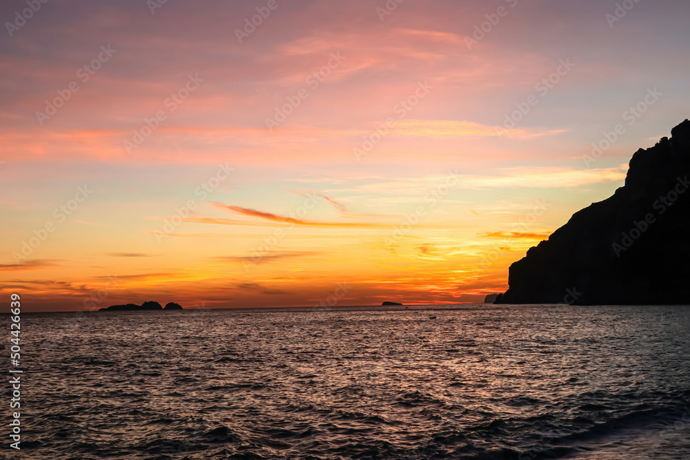 Panoramic sunset view from Marina Grande beach in Positano at Amalfi Coast, Italy, Campania, Europe. Silhouette of coastline. Orange twilight over Li Galli islands in Mediterranean Sea. Reflection