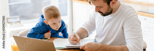 White father and son drawing and using laptop in kitchen at home