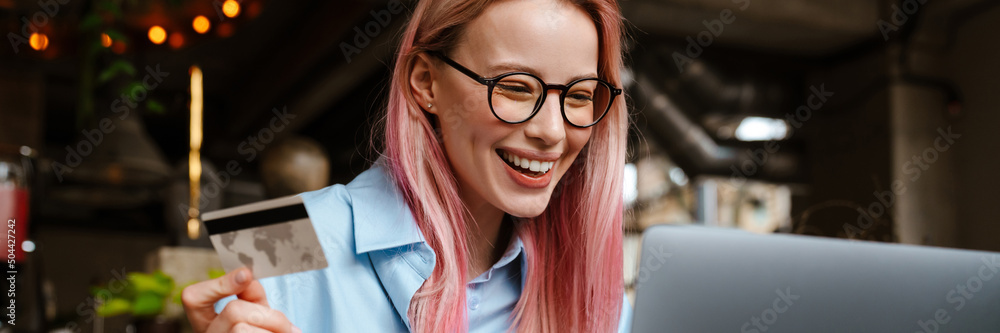 Young smiling woman using laptop and credit card while sitting in cafe Young smiling woman using laptop and credit card while sitting in cafe
