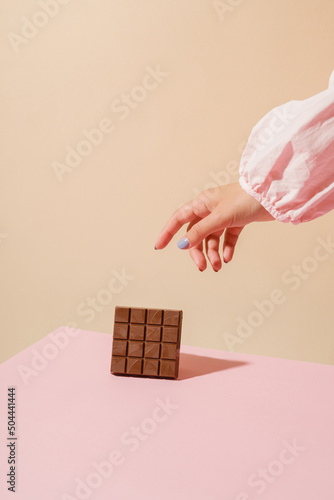 Milk chocolate on a beige-pink background. The girl's hand reaches for the chocolate. Creative chocolate photography. Sweet food