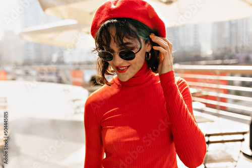 Close-up photo of beaming caucasian young lady with irreproachable smile outdoors. Lovely girl with shirt wavy hair in sunglasses and red cap. Travel, vacation and rest concept. photo