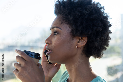 Young african american businesswoman holding coffee cup talking on smartphone
