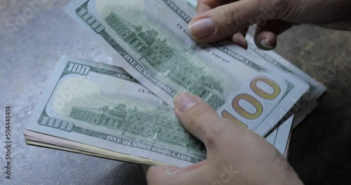 Dollars in female hands on background of wooden table. Woman counting 100 and 50 American dollar banknotes in arms. Lots of one hundred dollar bills. Banknotes on wooden table. Finance, economy, savin