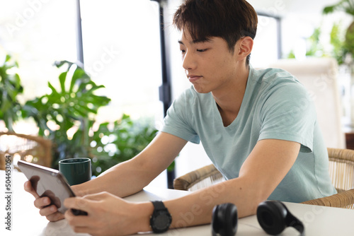 Asian teenage boy wearing blue t-shirt using digital tablet on table while sitting at home photo