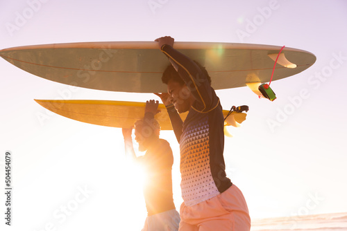 African american couple carrying surfboards on heads at beach against clear sky during sunset