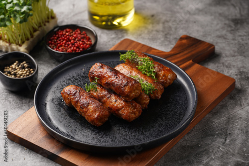 Traditional south european skinless sausages cevapcici made of ground meat and spices on black plate on dark wooden board, with thyme and watercress salad photo