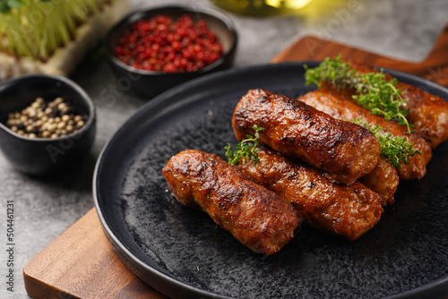 Traditional south european skinless sausages cevapcici made of ground meat and spices on black plate on dark wooden board, with thyme and watercress salad