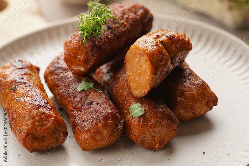 Traditional south european skinless sausages cevapcici made of ground meat and spices on white plate on light wooden board, with thyme and watercress salad