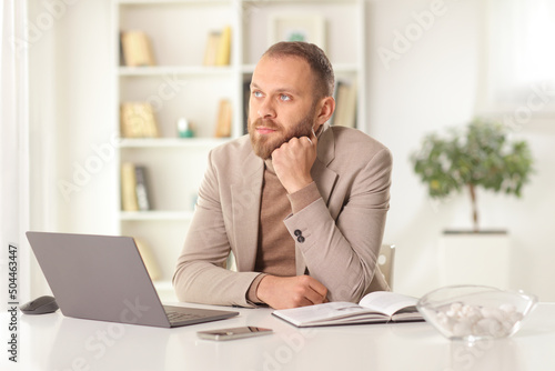 Pensive man sitting on a table at home with a laptop computer