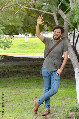 Young mexican man with beard and glasses saying hi in park