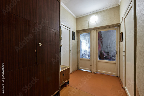 Example of Old Soviet Russian poor interior in Khruschev House. Aged  sideboard, table, chairs. Shabby floor. Tattered wallpaper on the wall. Apartment of pensioners. Selective focus. photo