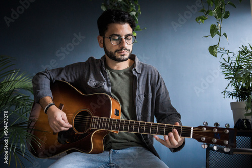 Young Musician Playing Classic Guitar Surrounded By Plants photo