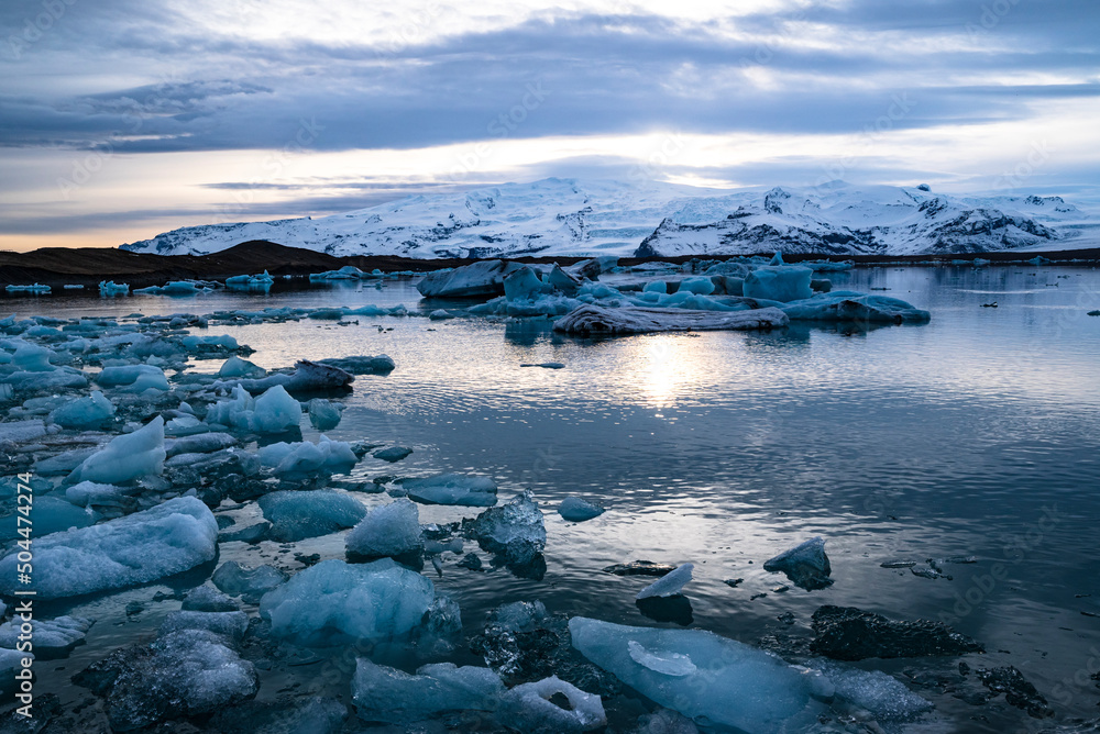 Scenic view over the icebergs in Jökulsárlón glacier lagoon under a dramatic sky, the evening sun reflected in the water, Öræfajökull in the background, Vatnajökull National Park, Route 1, Iceland