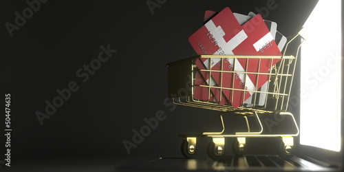 Bank card mockups with flags of Denmark in a small shopping cart on the laptop. 3D rendering