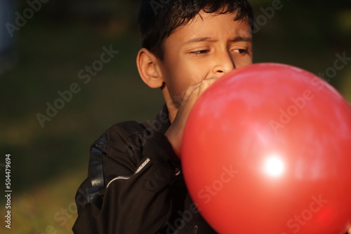 A little boy blowing a red balloon at outdoors in daytime photo