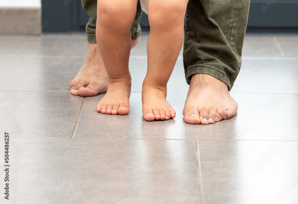 Cropped shot of an unrecognizable little boy learning to walk with his father behind his at home Cropped shot of an unrecognizable little boy learning to walk with his father behind his at home