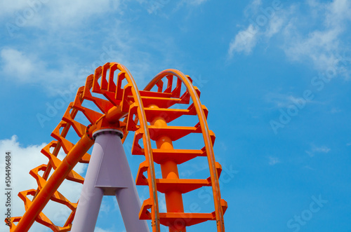 Curved of orange Roller Coaster track in close up isolated on blue sky background.