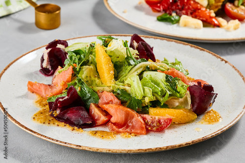 Healthy food - salmon salad with vegetables, greens and citrus. Summer salad with salmon, beetroot, orange and citrus dressing on concrete background. Summer menu in minimal style. Aesthetic food.