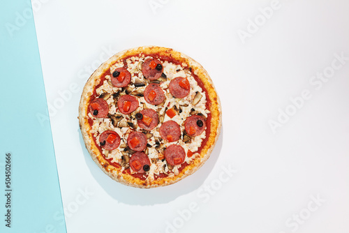 Italian pizza with salami, mushroom, black olives on coloured background. Meat pizza with salami and olives minimal style on blue and purple color. American pizza delivery concept with color backdrop