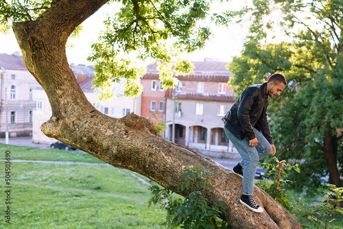 guy poses sitting on the branch of a big tree photo