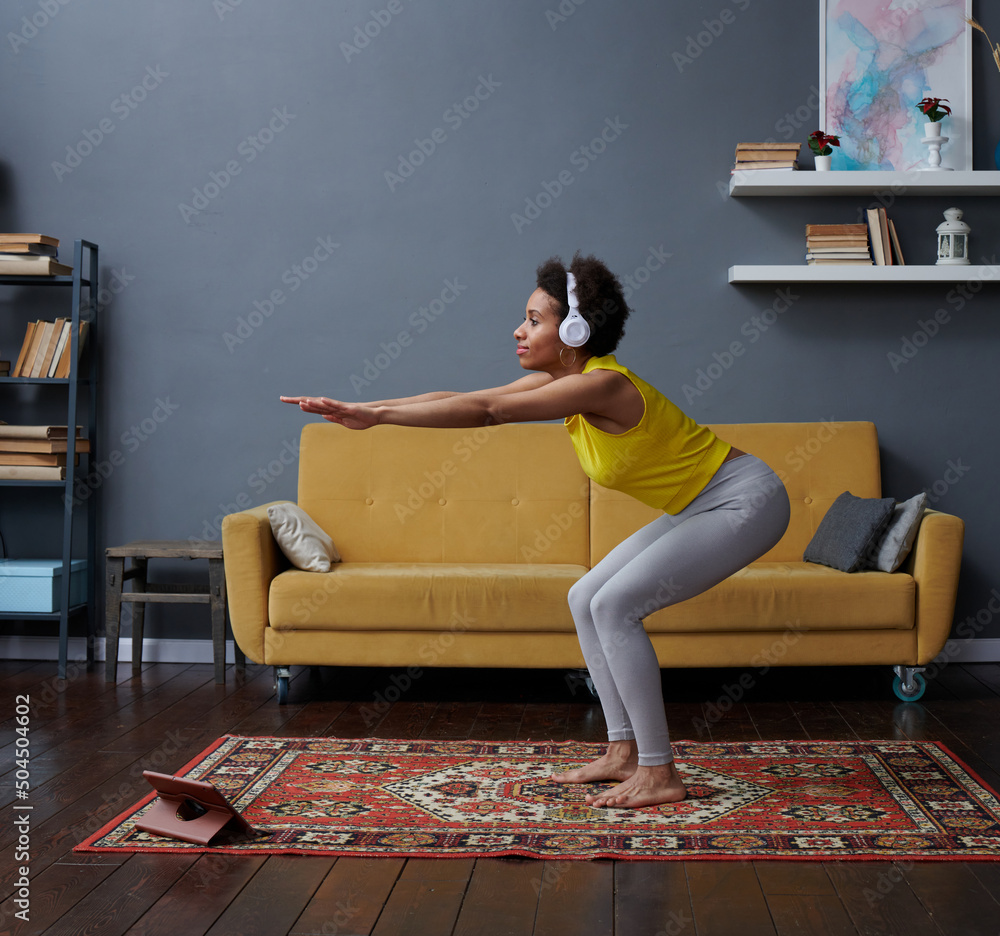 © Elena Kharichkina/Stocksy - A woman in headphones does exercises at home