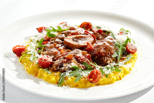 Traditional Italian dish - osso buco with risotto Milanese and cherry tomato and rucola. Ossobuco with saffron rice isolated on white background. Stewed meat on bone with yellow risotto. photo