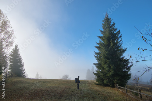Small figure of lonely hiker enjoying his time on wild forest trail on foggy autumn day