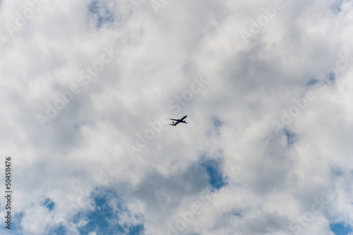 The plane is flying high in the sky under the clouds