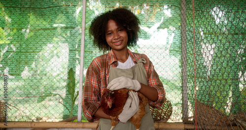 Young african america happy female farmer is caressing with love and care ecologically grown hen for biological genuine food products industry in hay barn of countryside agricultural farm.