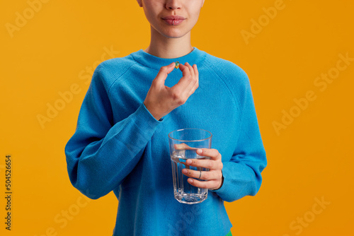 Crop teenager taking pill with water photo