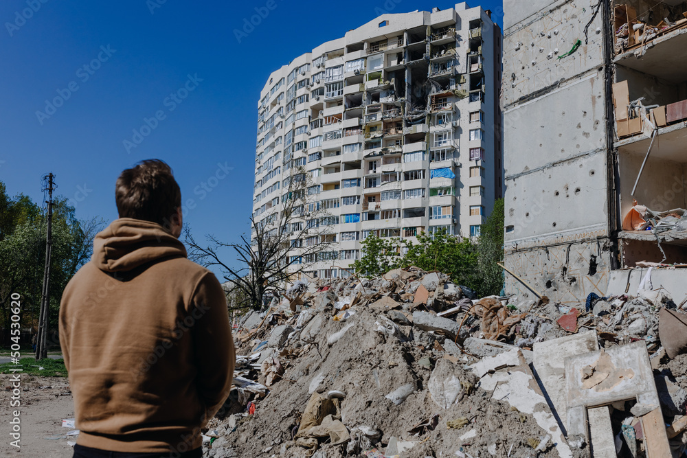 Chernihiv Ukraine 2022: a guy looks at the ruins after an air strike. Rear view. The building was destroyed after the air strike. Ruins during Russia's war against Ukraine. - obrazy, fototapety, plakaty 