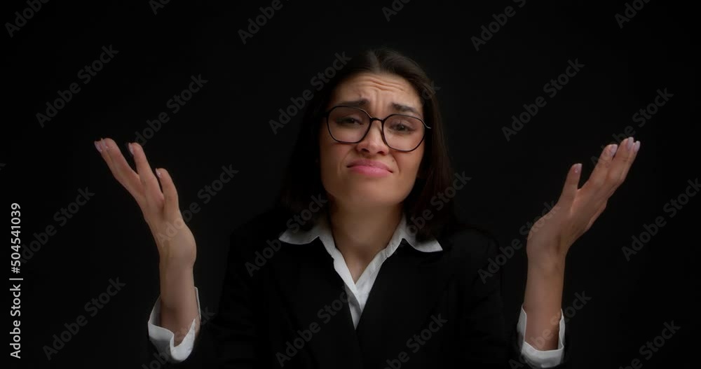 Sad businesswoman on an isolated black background stands with her palms raised and sighs, well, why did this happen. An Asian woman in glasses and office clothes is very upset. Sad businesswoman on an isolated black background stands with her palms raised and sighs, well, why did this happen. An Asian woman in glasses and office clothes is very upset.
