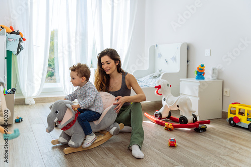 Cute boy on rocking toy in playroom with mother photo