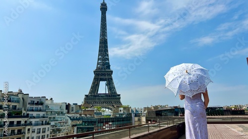 a beautiful young girl in a summer dress stands against the backdrop of the Eiffel Tower with a lace umbrella, she raised her hand and as if taking off there is a place for advertising travel agency.