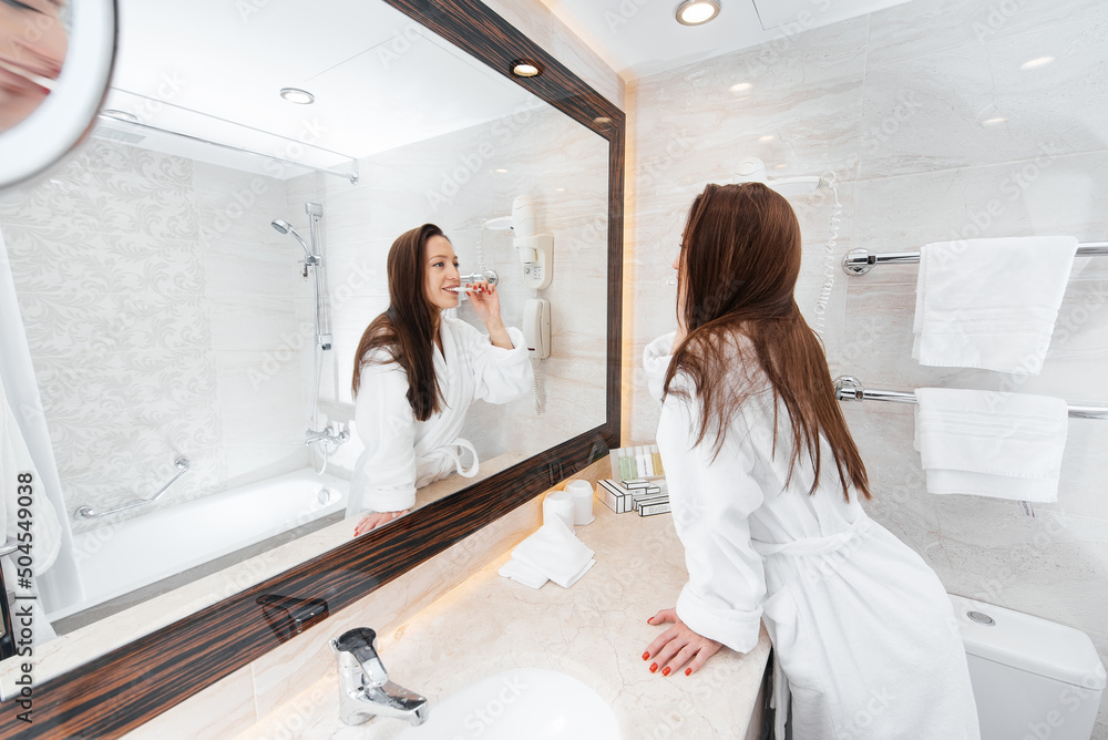 A young beautiful girl is brushing her teeth in a beautiful white bathroom. A fresh good morning at the hotel. Rest and travel. Hotel recreation, and tourism. A young beautiful girl is brushing her teeth in a beautiful white bathroom. A fresh good morning at the hotel. Rest and travel. Hotel recreation, and tourism.