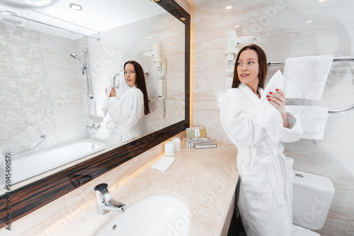 A young beautiful girl washes her face and holds a towel in a beautiful white bathroom. A fresh good morning at the hotel. Rest and travel. Hotel recreation, and tourism.